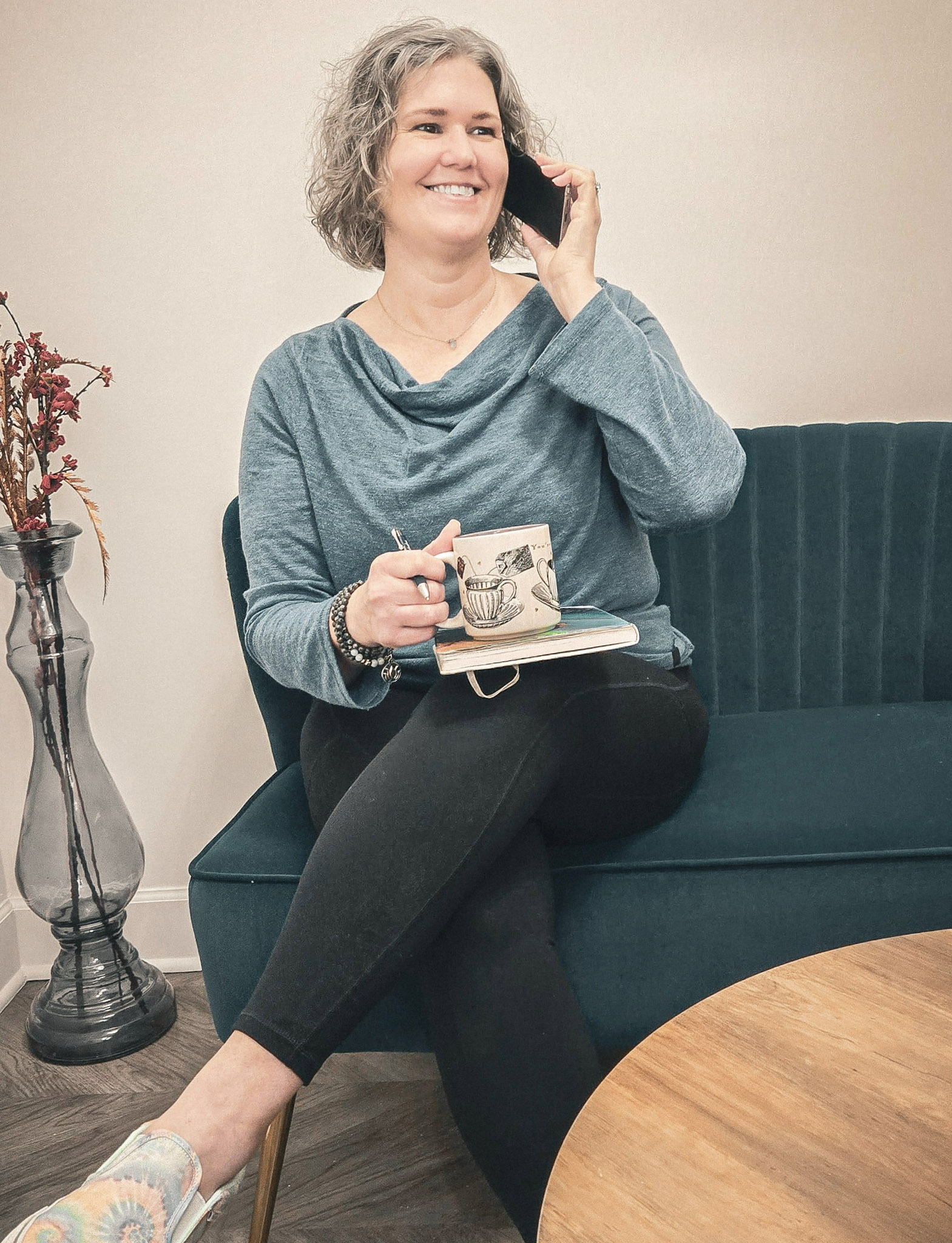 Meg Claudio, Holistic Mind-Body Practitioner & Coach, smiling while on a call with tea in hand, seated in a calming wellness space