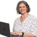 Meg Claudio, Holistic Mind-Body Practitioner, smiling while working on a laptop