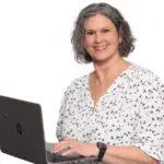Meg Claudio, Holistic Mind-Body Practitioner, smiling while working on a laptop